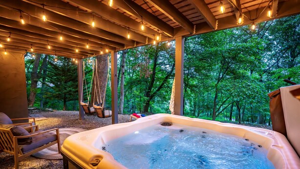 A hot tub with a view of a forest, a wooden chair, and string lights. - Family Base Camp + 5BR + Game Room + Hot Tub (McGaheysville)