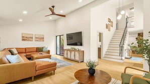 A spacious living room with a large sectional sofa, a flat-screen TV, a wooden cabinet, and a staircase leading to an upper level. - Family Base Camp + 5BR + Game Room + Hot Tub (McGaheysville)