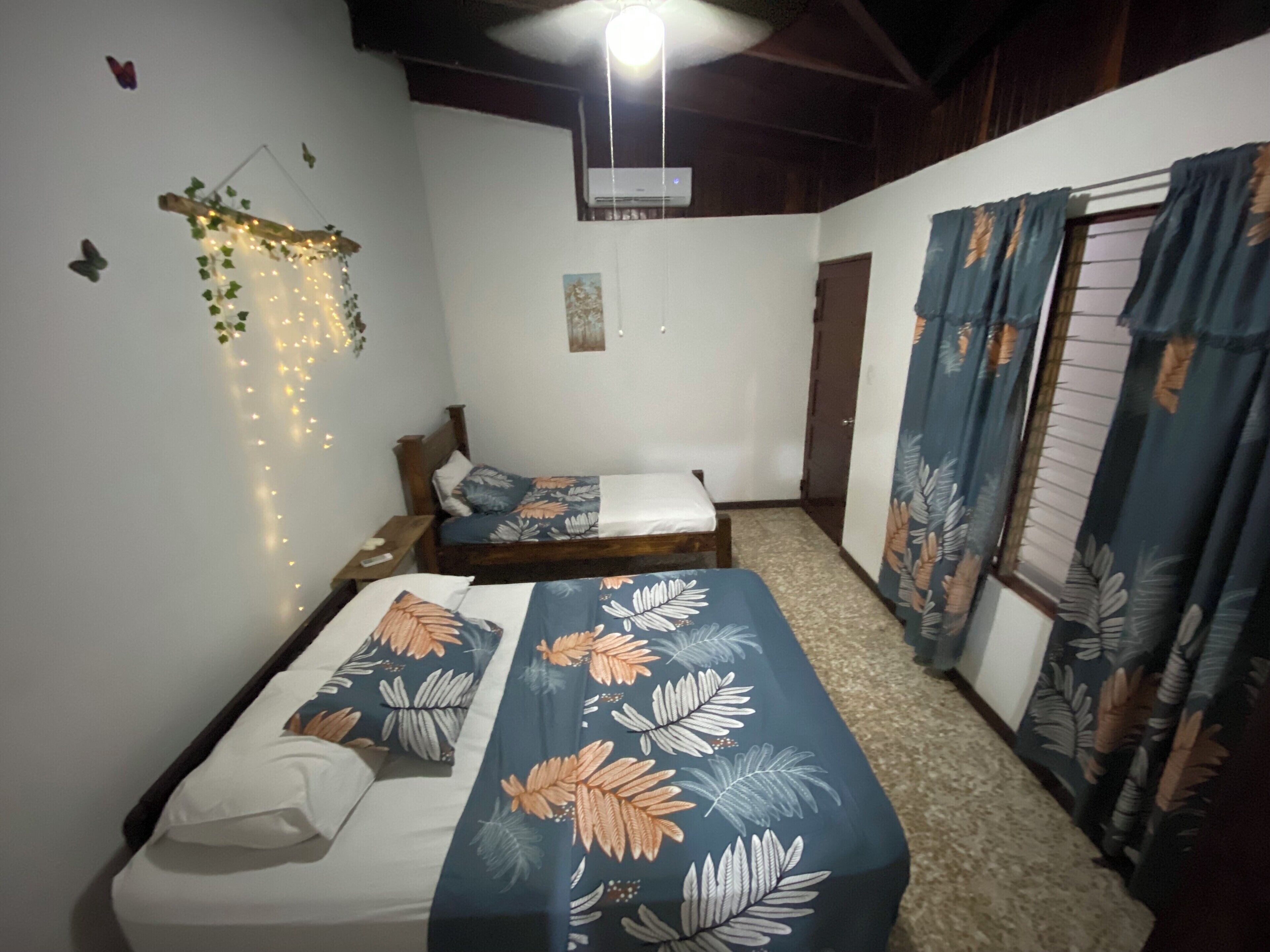Un dormitorio con dos camas, ventilador de techo y aire acondicionado instalado en la pared.