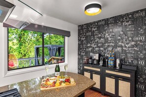A kitchen with a breakfast bar, a coffee station, and a view of greenery outside. - Asheville 6BR Retreat — Bowling Alley, Hot Tub, Sauna, Theater | Sleeps 16 (Asheville)