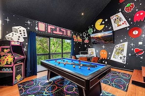 Een pooltafel in een kamer met uitzicht op bomen, een dartbord en spelautomaten.