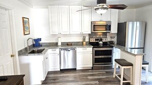 A kitchen with white cabinets, stainless steel appliances, a dishwasher, a stove, and a ceiling fan.