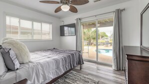 A bedroom with a bed, a ceiling fan, a TV, and a view of a pool.
