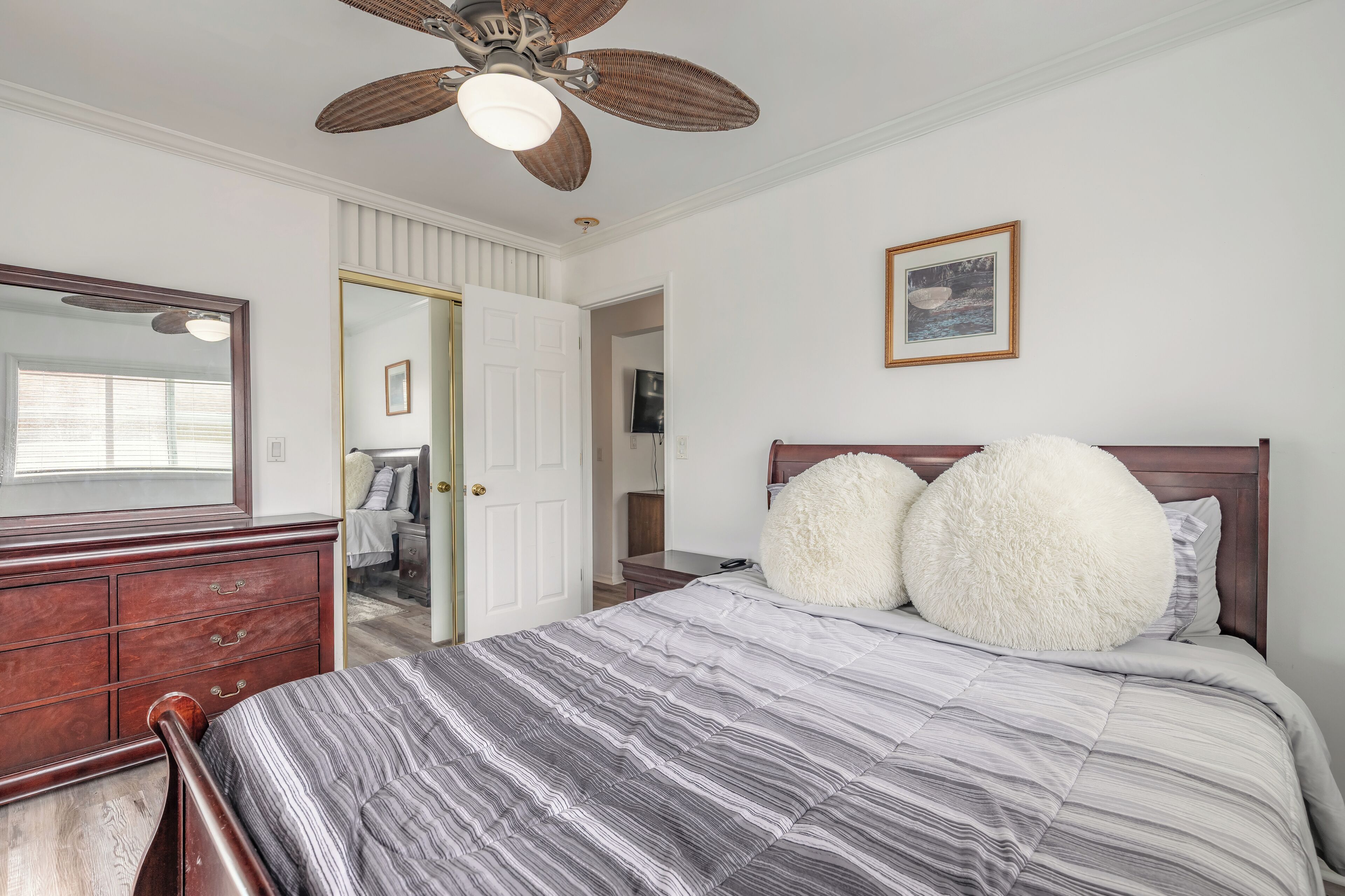 A bedroom with a large bed, a wooden dresser, a ceiling fan, and a framed picture on the wall.