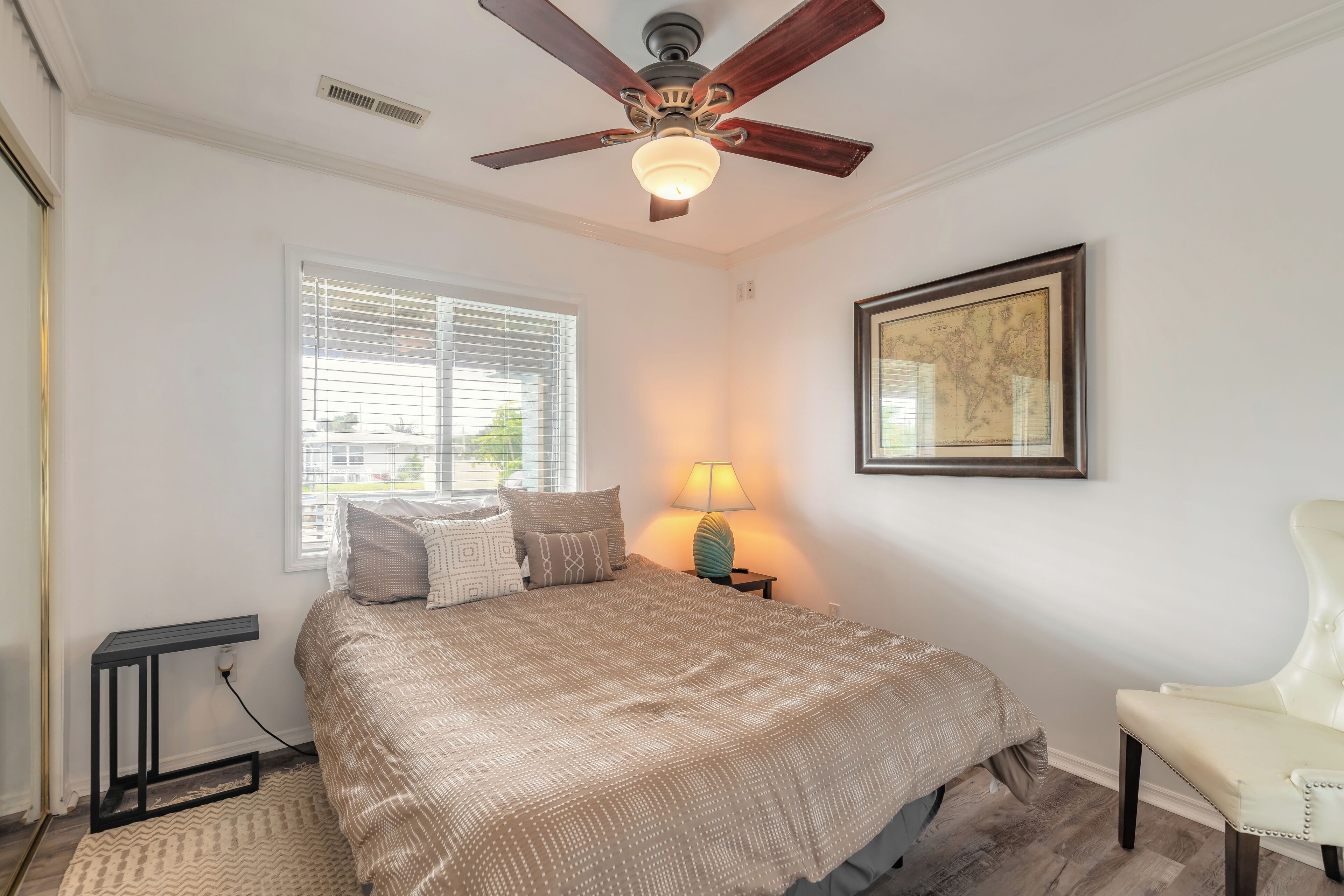 A bedroom with a bed, a standing lamp, a chair, a window, and a ceiling fan.