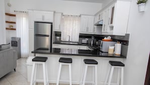 A modern kitchen with white cabinets, a black countertop, and three white bar stools. - Luxury Caribbean 5BR Villa – Private Pool, BBQ & Ocean Breezes (Sosúa)