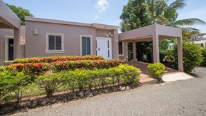A modern building with a flat roof, a covered entrance, and a well-maintained garden with various shrubs and flowers. - Luxury Caribbean 5BR Villa – Private Pool, BBQ & Ocean Breezes (Sosúa)