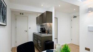 A compact kitchen with modern appliances, a dining area with a table and chairs, and a small potted plant. - GuestReady - Prime location near Greenwich Park (London)