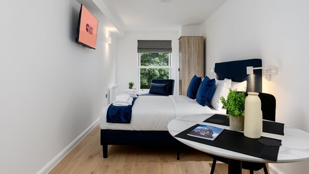 A modern hotel room with a bed, bedside table, and a view of greenery outside. - GuestReady - Prime location near Greenwich Park (London)