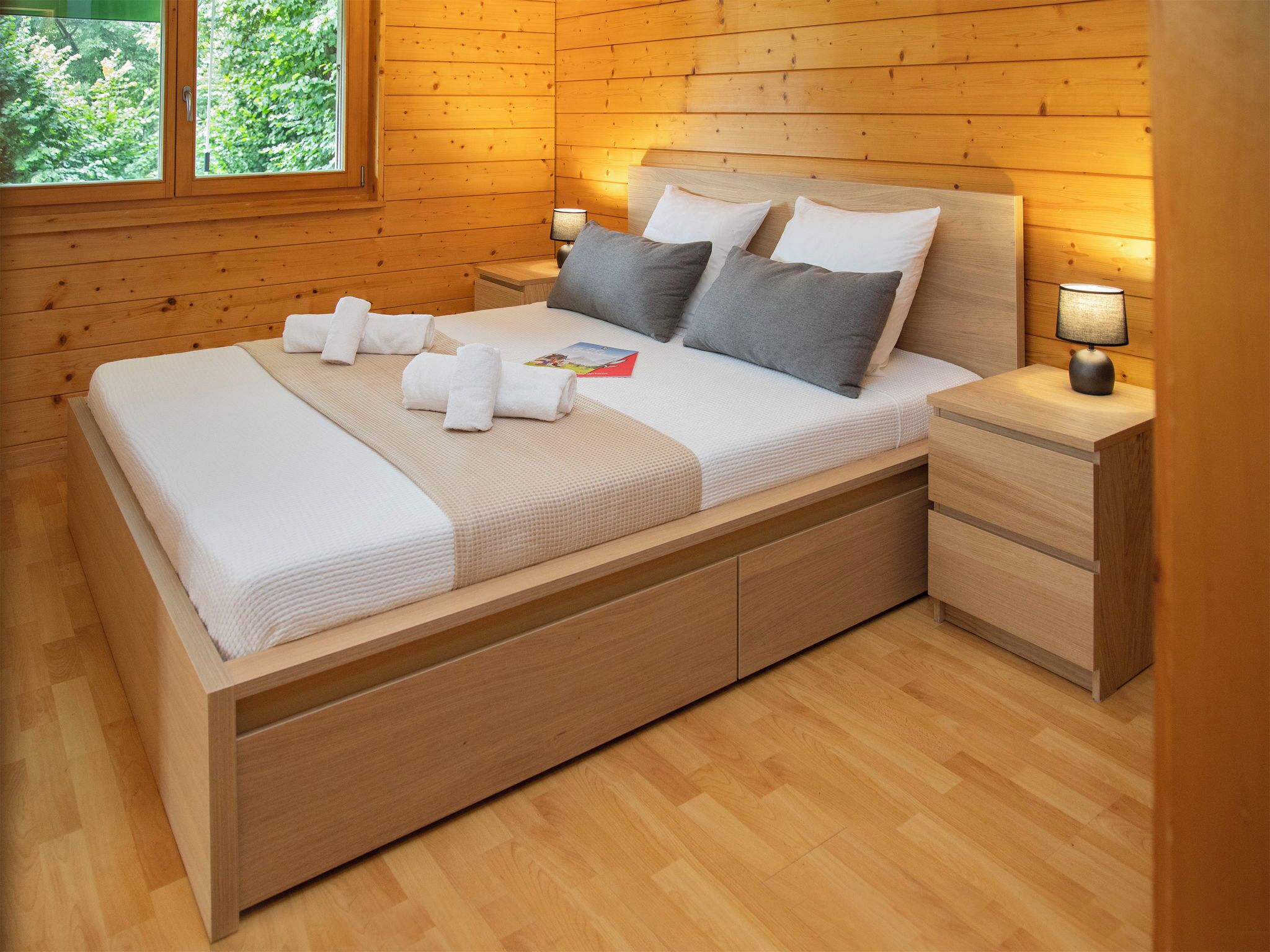 A wooden-paneled bedroom with a bed, bedside tables, and a window.