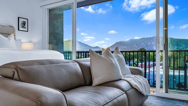 Una habitación de hotel moderna con una cama grande, un sofá de cuero y un balcón con vistas a la montaña.