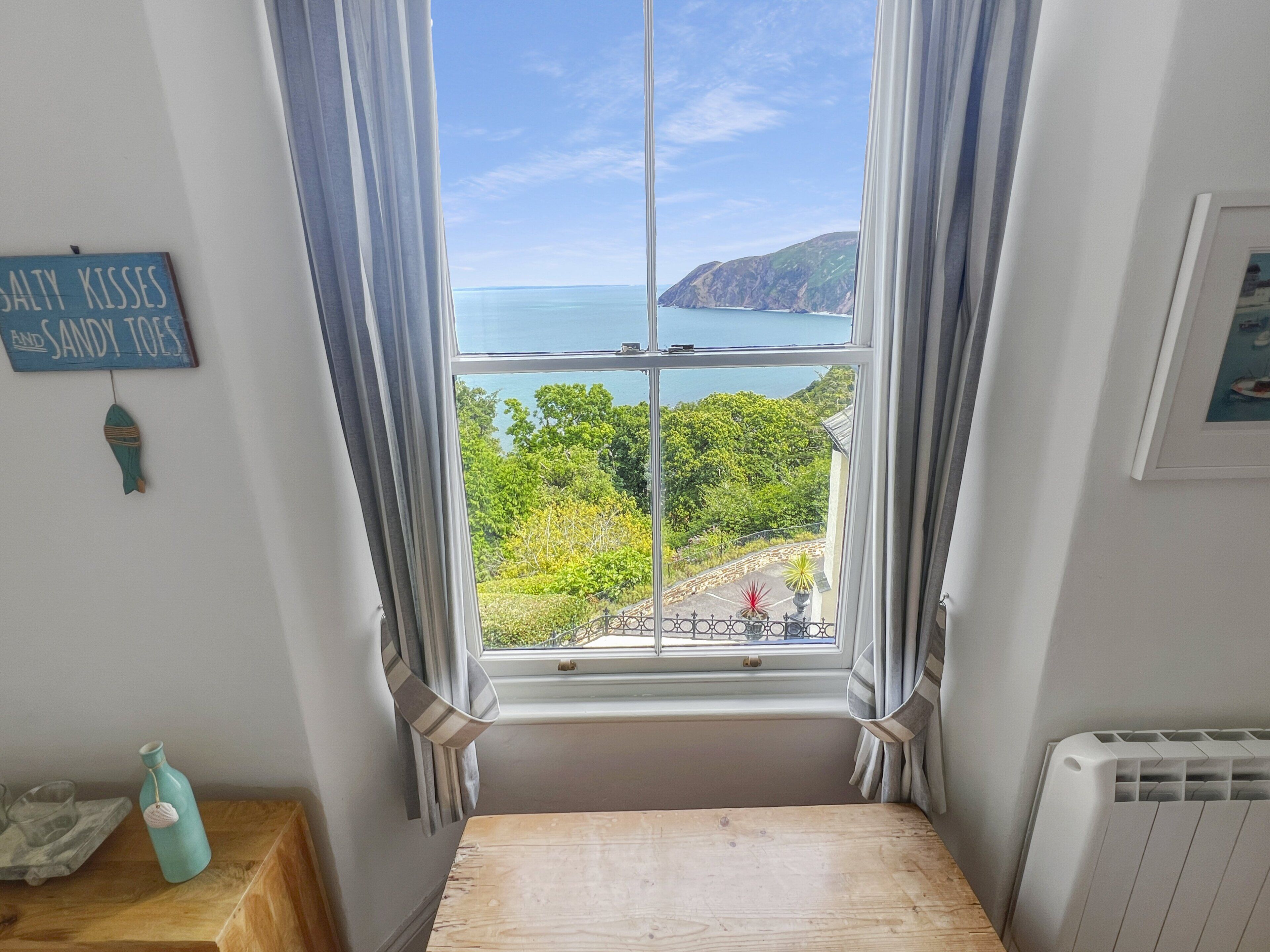 Una habitación con vistas al mar, una ventana con cortinas, un banco de madera y una pared con un letrero.