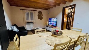 A dining area with a wooden table and chairs, a television in the background, and a Christmas tree. - Adorable traditional and functional Farm House. (Guia)