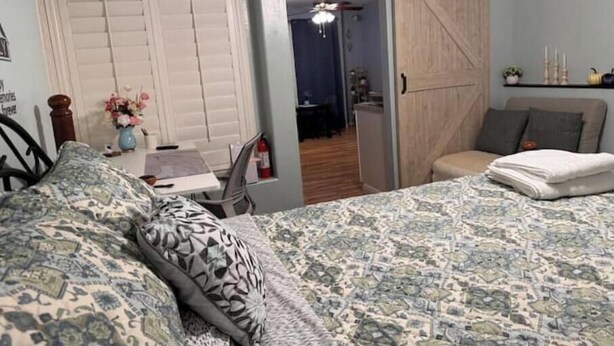 A bedroom with a bed, a desk, a chair, a wardrobe, and a door leading to another room.