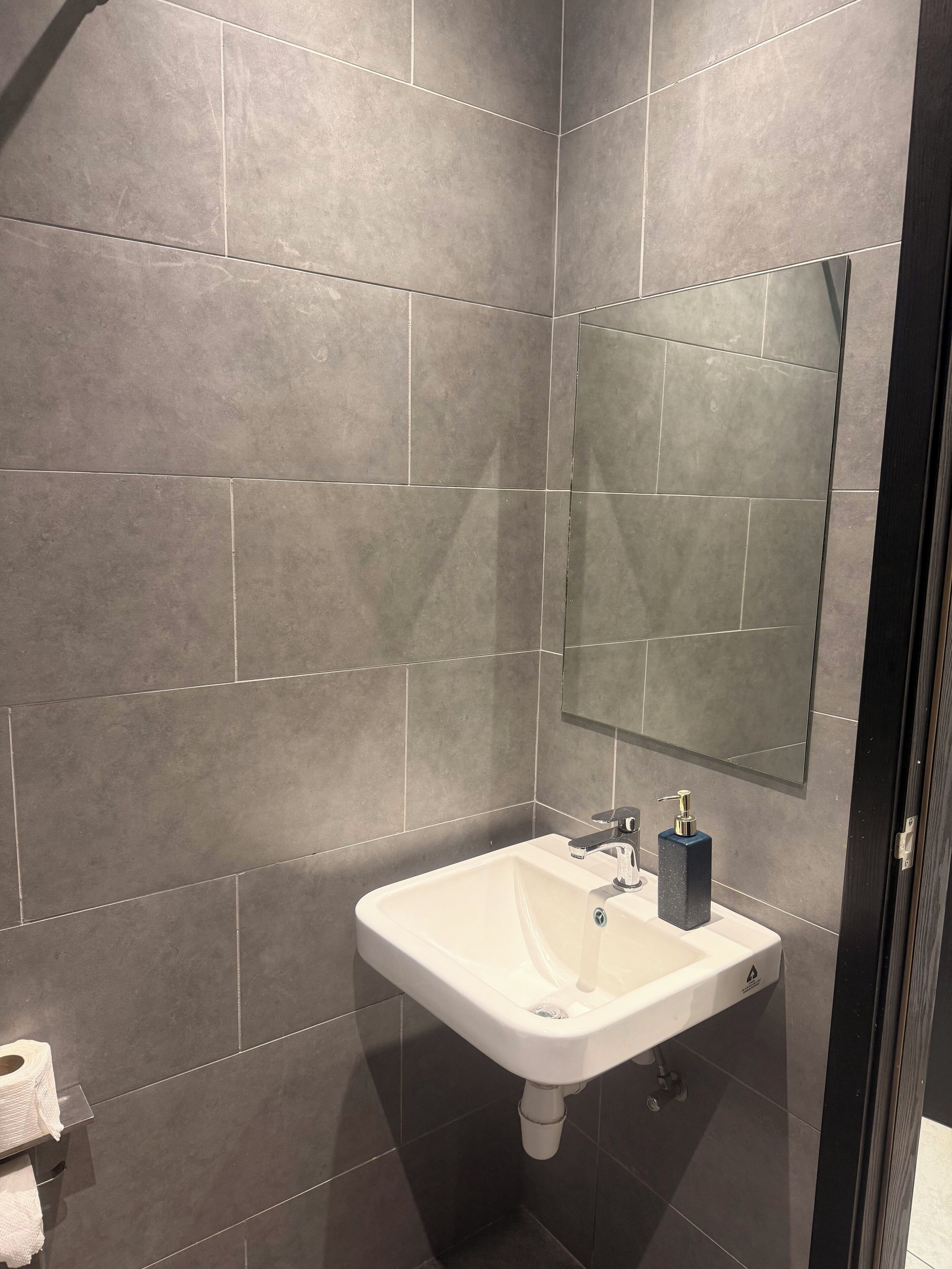 Un baño con lavamanos blanco, baldosas gris oscuro, un espejo y un perchero para toallas.