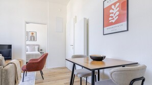 Een moderne hotelkamer met een houten vloer, een eettafel met stoelen, een televisie en een bed met een witte kap.