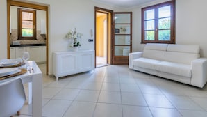 A spacious living area with a white sofa, a dining table set with plates and a glass, and a kitchen visible through an open door.