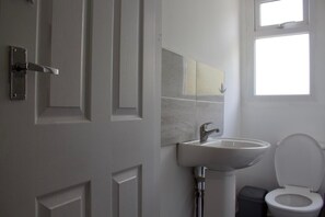 Ein Badezimmer mit einer weißen Tür, einem Waschbecken, einer Toilette und einem Fenster.