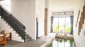 Un interior moderno con una escalera, una zona de piscina y vistas a un paisaje verde.