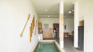 Un pasillo estrecho con una piscina pequeña, armarios de madera, un refrigerador y una zona de comedor con una banca.