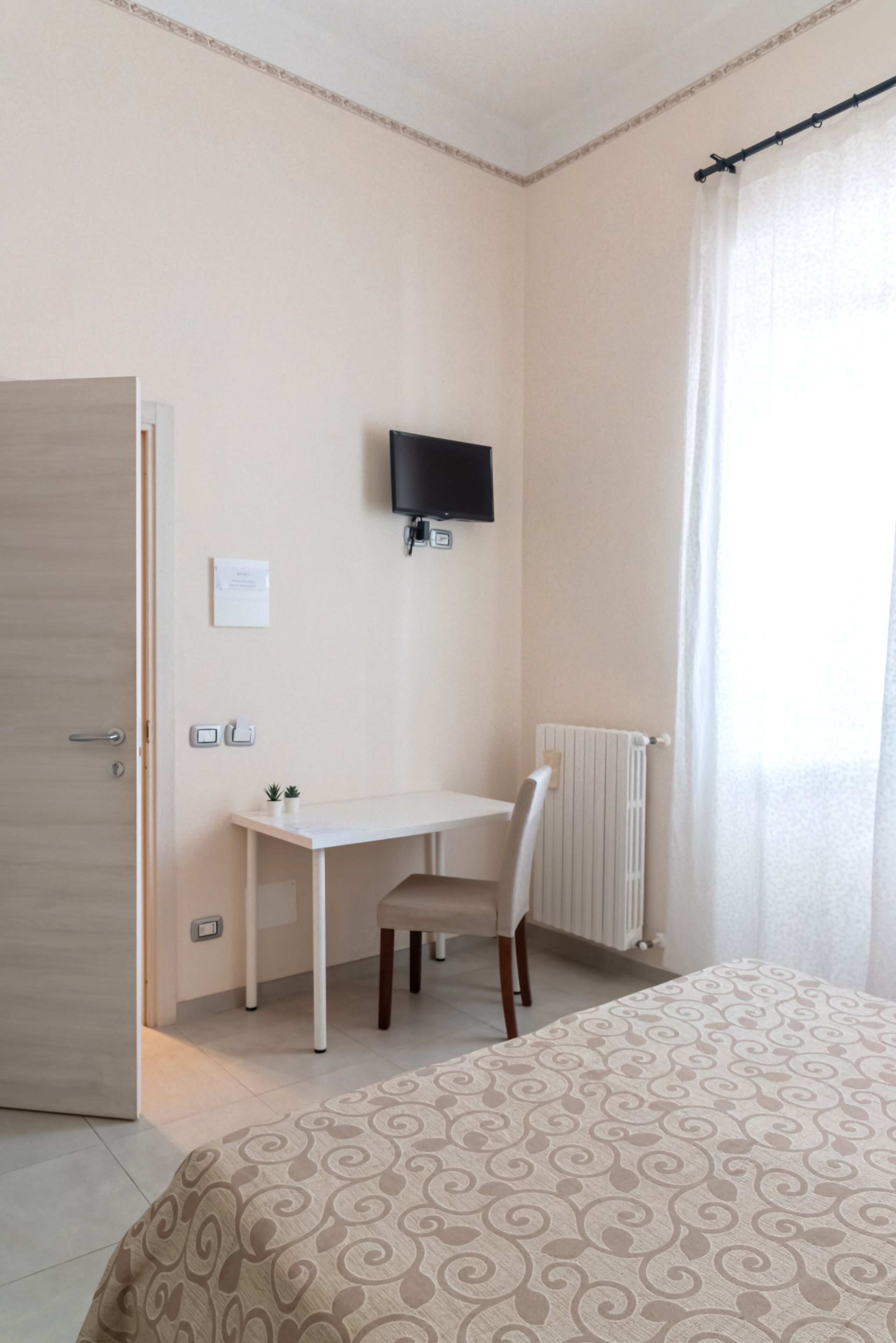 A bedroom with a bed, a desk, a chair, a television, and a window with curtains.