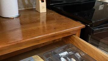 A kitchen with a wooden countertop, a black stove, and a drawer with utensils.