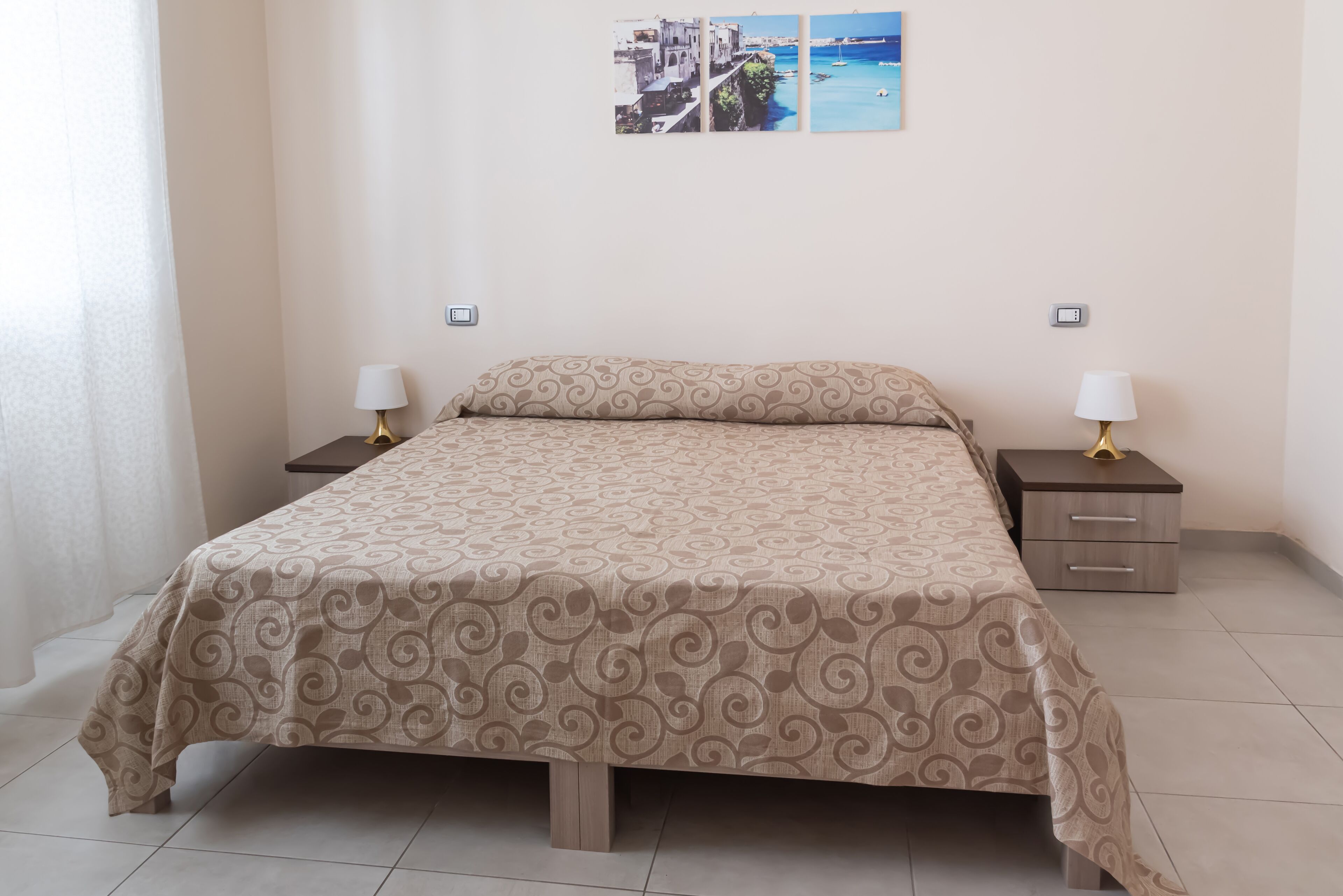 A neatly made bed with a patterned bedspread, two bedside tables with lamps, and a wall-mounted power outlet.