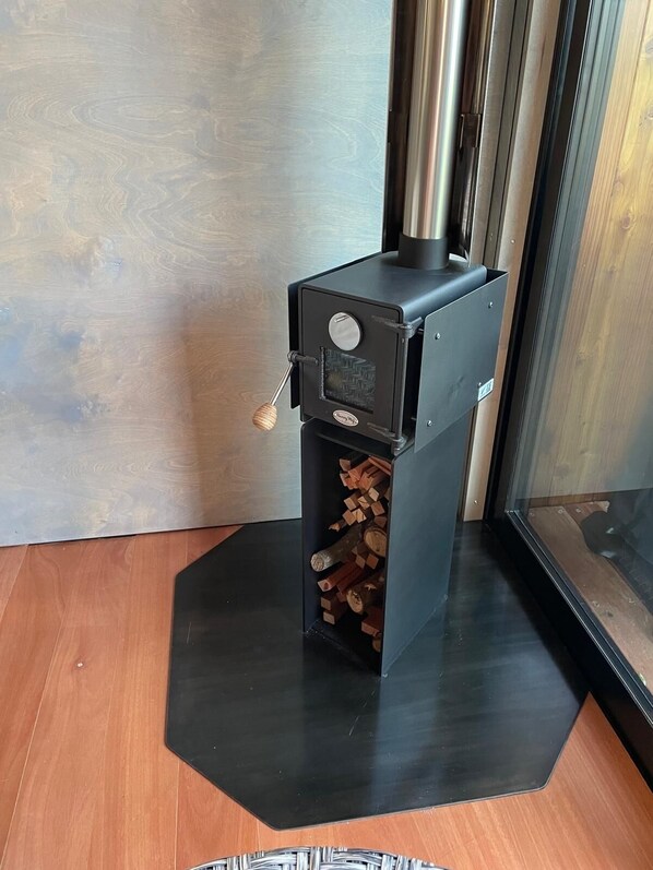 A wood stove with a handle, a metal chimney, and a black base. - Reelhaus Retreat (Okiato)