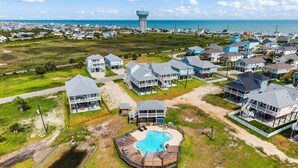 An aerial view of a coastal residential area with houses, a large swimming pool, and a water tower in the background. - Terramar Beach Escape + Easy Beach Access (Galveston)