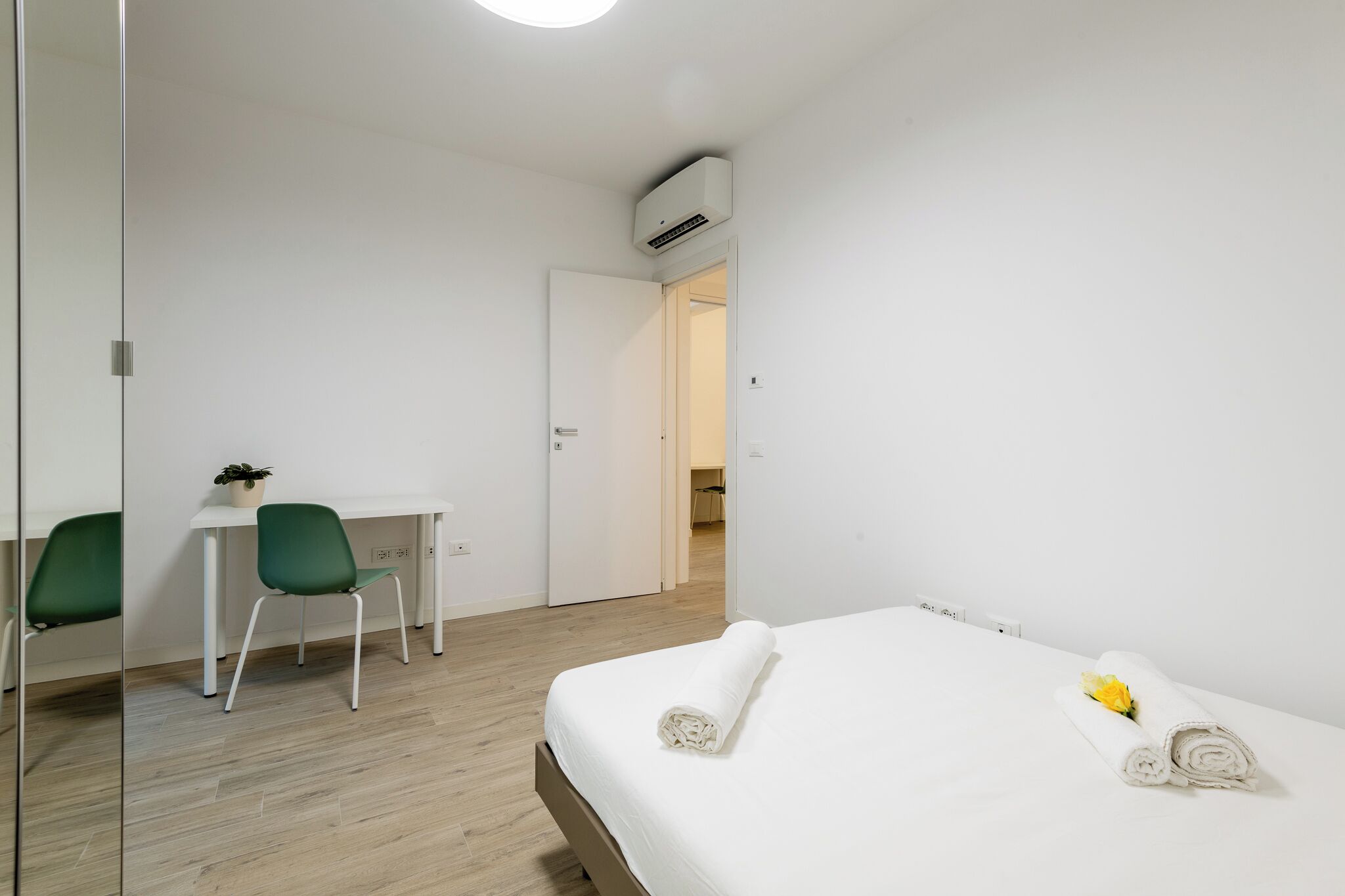 A hotel room with a bed, a desk, a chair, and a small plant.