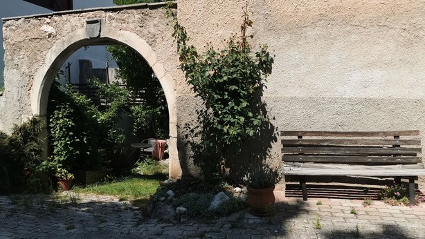 Un espace extérieur agrémenté d’une arche en pierre, d’un banc en bois et d’une plante en pot.