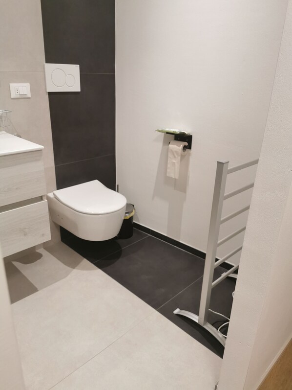 Une salle de bain moderne avec des toilettes blanches, un lavabo et un porte-serviettes.