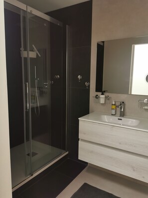 A modern bathroom with a glass-enclosed shower, a white vanity with a mirror, and a dark floor. - Lavender House Small apartment made from an old village house (Sarnonico)