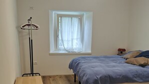 Une chambre à coucher avec un lit, un bureau, une lampe sur pied et une fenêtre avec des rideaux.