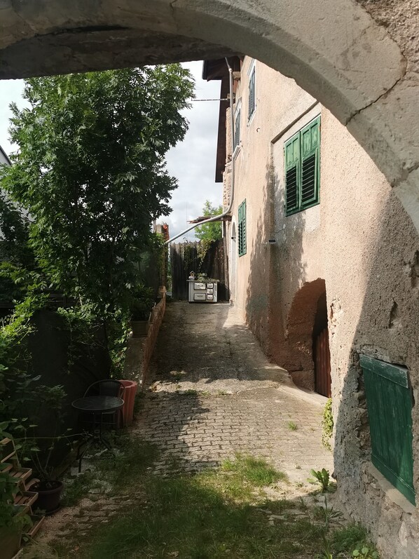 A narrow cobblestone alleyway with a rustic building on one side, a tree on the other, and a small outdoor seating area with a table and chairs. - Lavender House Small apartment made from an old village house (Sarnonico)