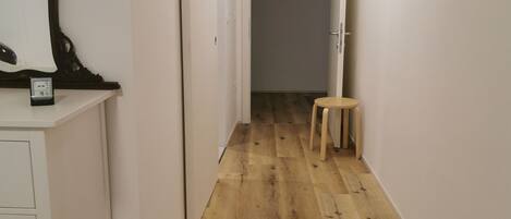A narrow hallway with wooden flooring, white walls, and a small stool.