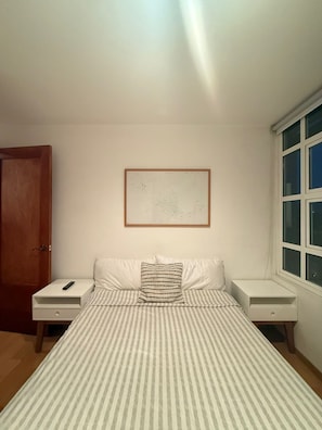 A bedroom with a bed, two nightstands, a framed map on the wall, a window, and a door. - Frida my Loft (Mexico City)
