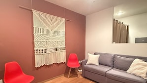 Ein modernes Wohnzimmer mit einem grauen Sofa, zwei roten Sesseln, einem Wandbehang aus Makramee und Holzboden.