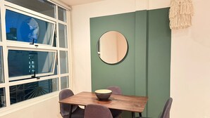 Een eethoek met een houten tafel, vier stoelen, een schaal en een ronde spiegel aan een groene wand.