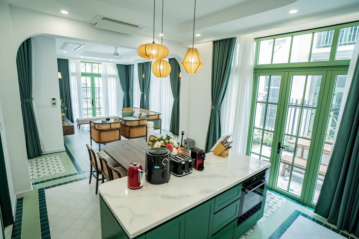 A modern kitchen with a central island, green cabinets, and a dining area with a wooden table and chairs.