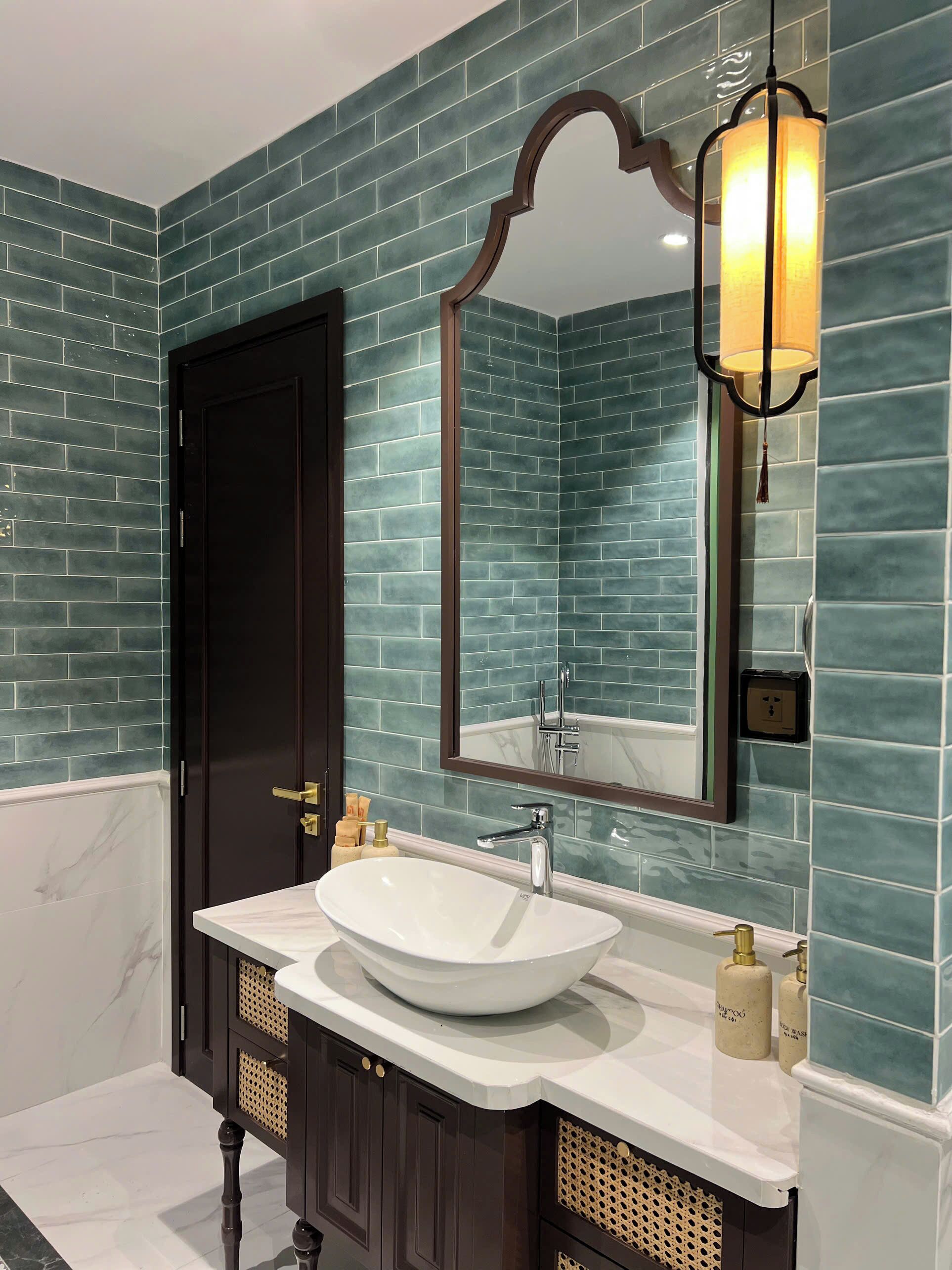 A bathroom with a white sink, dark wooden cabinets, and teal-tiled walls.