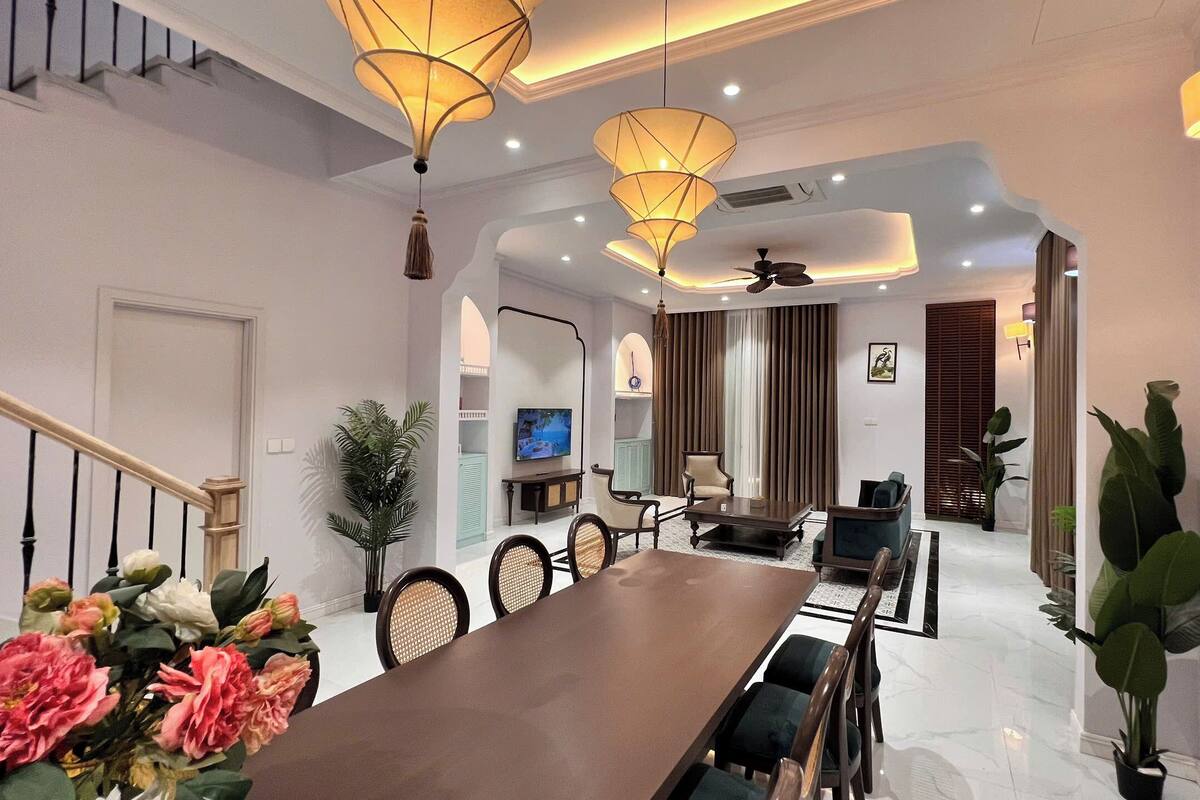 A modern dining area with a long table, chairs, and hanging lamps.