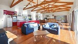 A spacious living area with a kitchen, two sofas, a dining table, and a high ceiling with exposed beams.