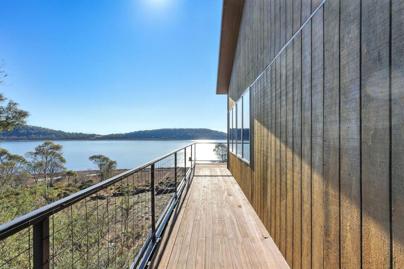 A wooden deck with a metal railing overlooking a lake and hills.