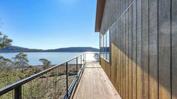 A wooden deck with a metal railing overlooking a lake and hills.