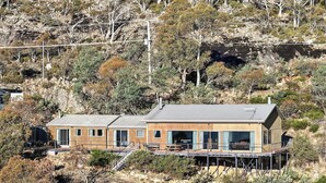 A two-story house with a deck, surrounded by dry vegetation and trees.