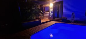 Ein Poolbereich mit Whirlpool, Holzterrasse und überdachter Sitzgelegenheit mit Tisch und Stühlen.