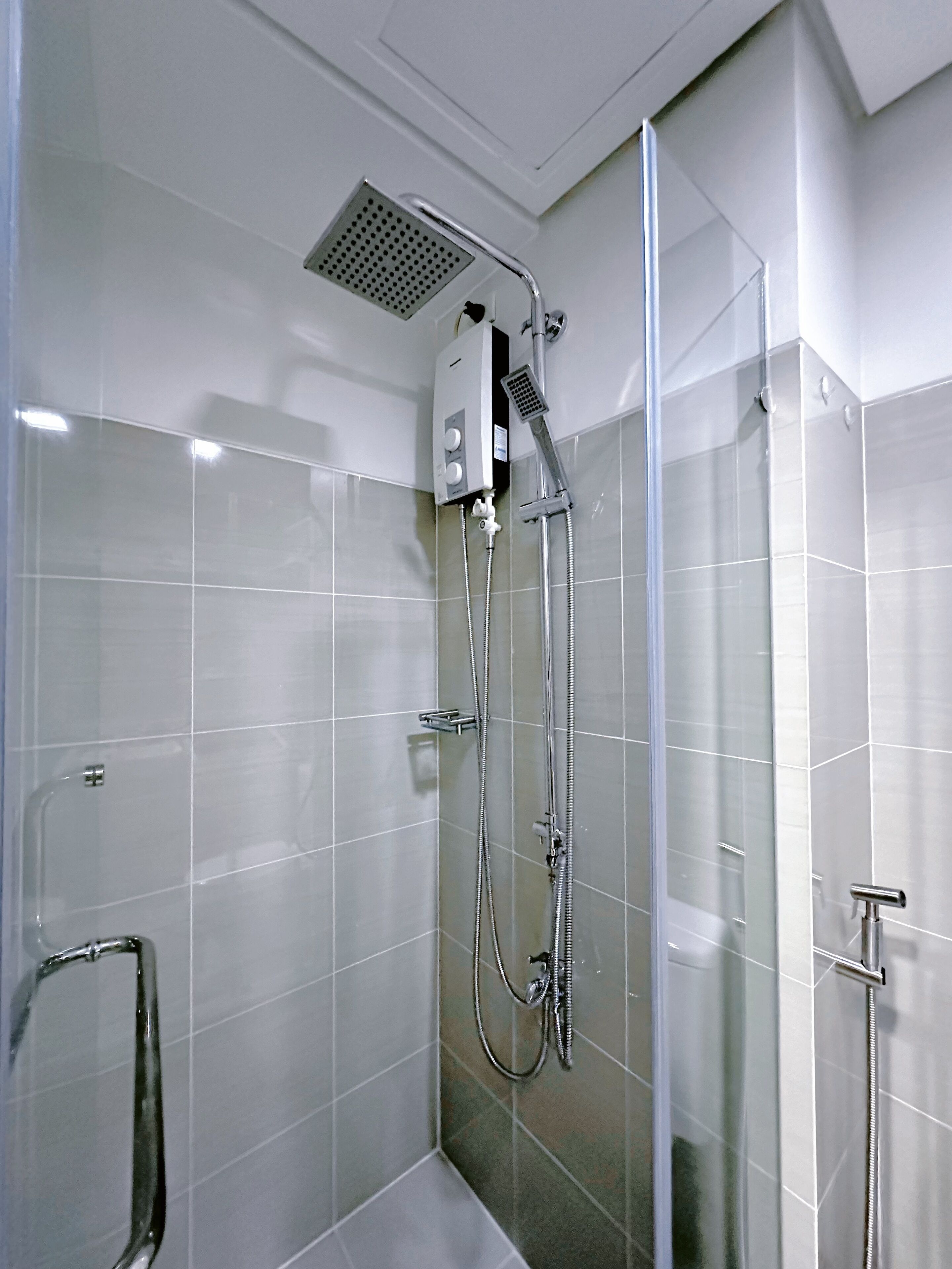 Un área de ducha moderna con mampara de vidrio, cabezal de ducha manual y panel de control en la pared.