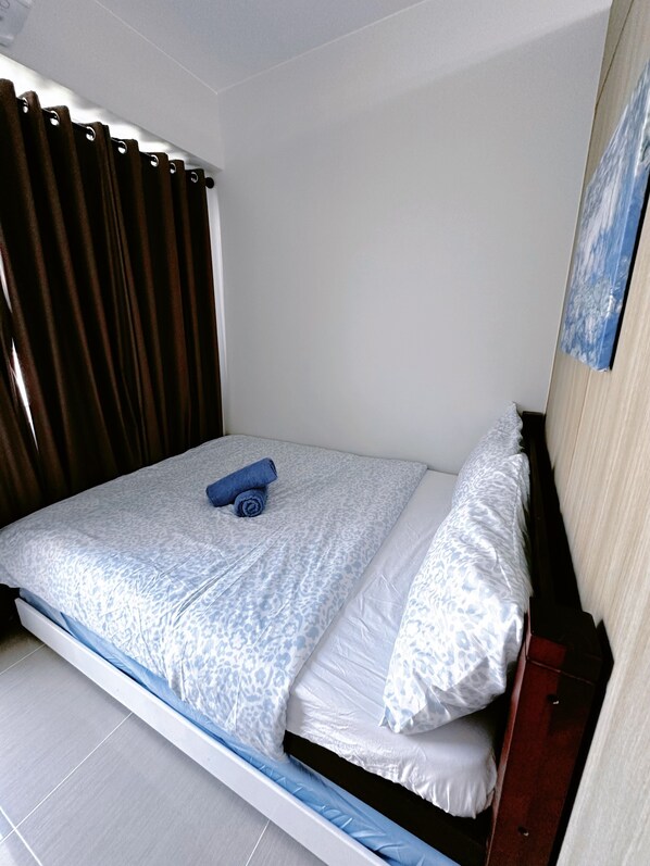 Ein Einzelbett mit einem gemusterten Bettbezug, ein gerolltes Handtuch und ein Kopfkissen.