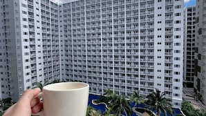 Una mano che tiene una tazza con vista su edifici residenziali e un'area verde con palme.